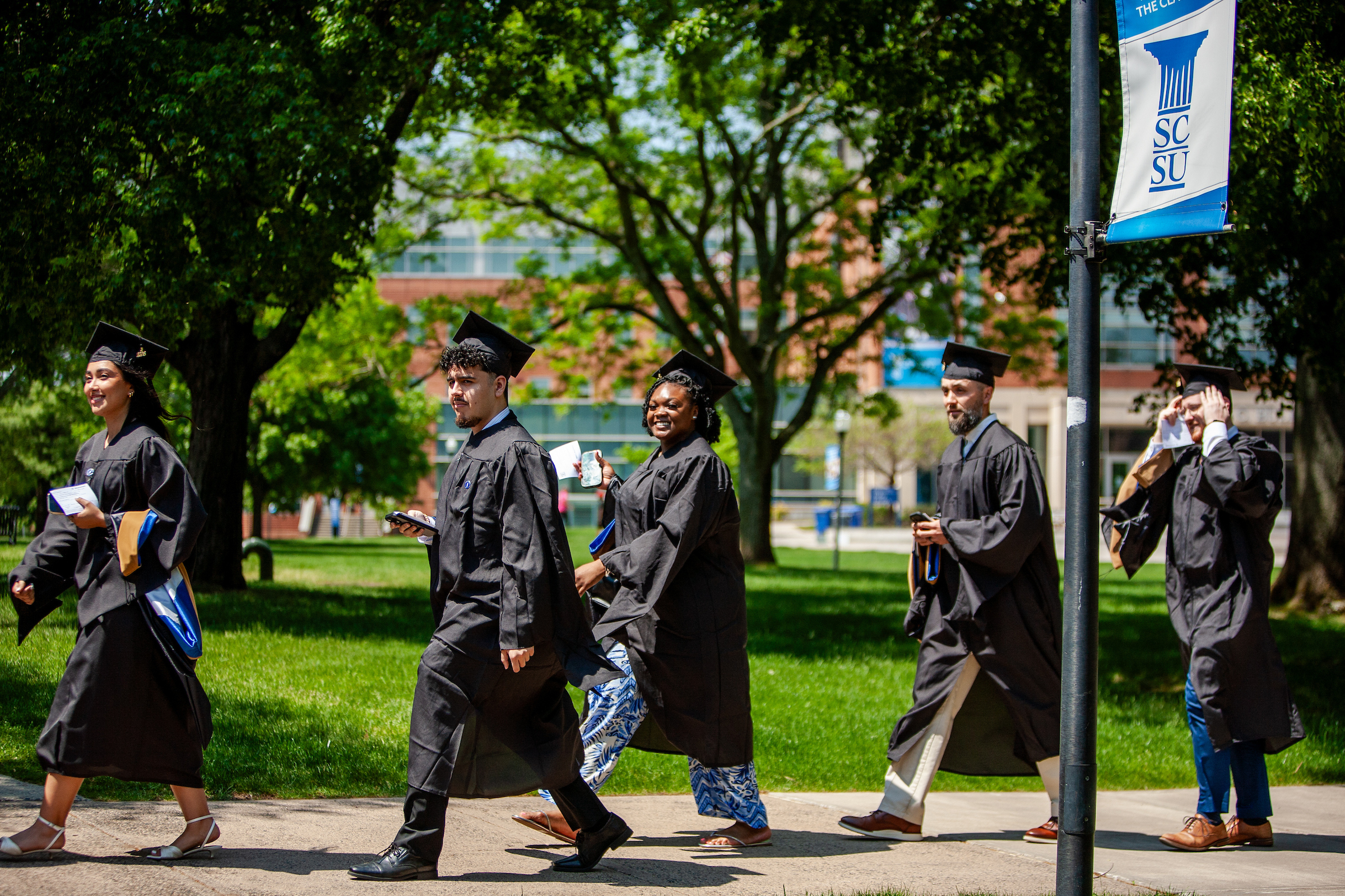 students in graduation regalia walking on the quad.
